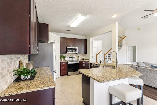 kitchen with a breakfast bar, sink, ceiling fan, stainless steel appliances, and light stone countertops