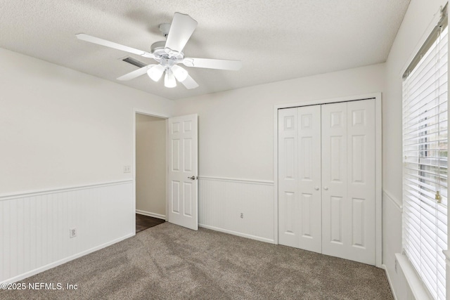 unfurnished bedroom with dark colored carpet, ceiling fan, a textured ceiling, and a closet