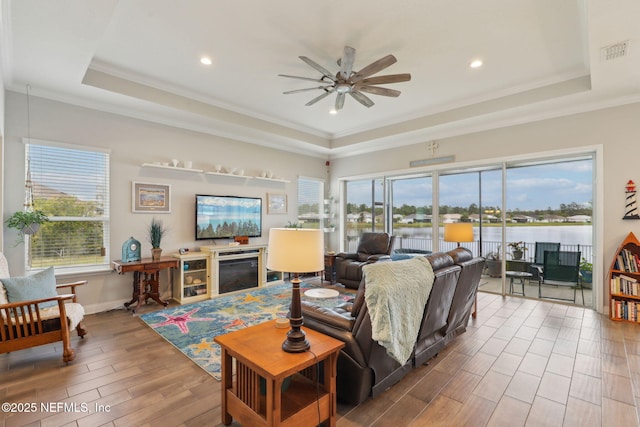 living area featuring visible vents, ornamental molding, a ceiling fan, wood finished floors, and a raised ceiling