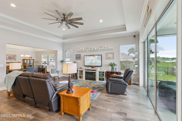 living area with crown molding, ceiling fan with notable chandelier, a fireplace, wood finished floors, and a raised ceiling