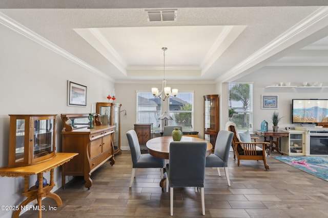 dining area featuring visible vents, a notable chandelier, a tray ceiling, crown molding, and wood tiled floor