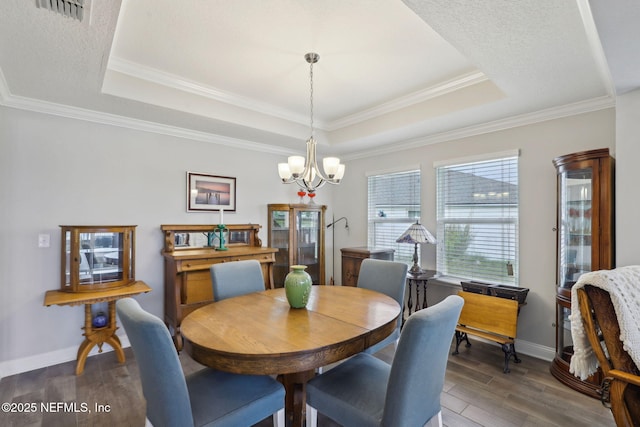 dining area with a tray ceiling, visible vents, wood finished floors, and a chandelier