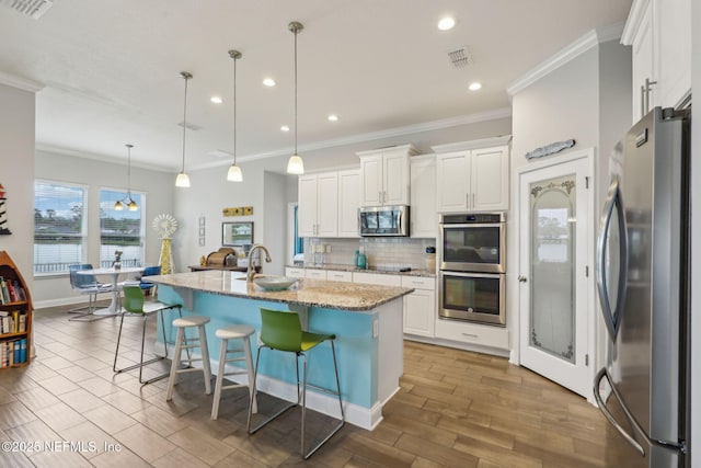 kitchen featuring tasteful backsplash, light stone counters, white cabinets, stainless steel appliances, and a sink