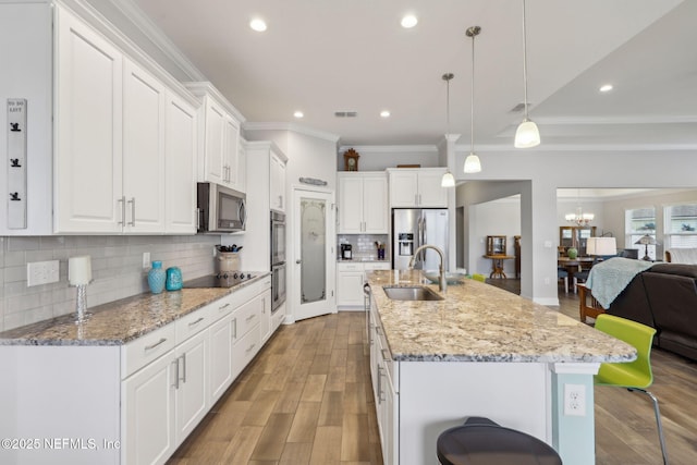 kitchen featuring open floor plan, light wood-style floors, white cabinets, stainless steel appliances, and a sink