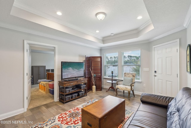 living area with crown molding, baseboards, a tray ceiling, light wood-style floors, and a textured ceiling