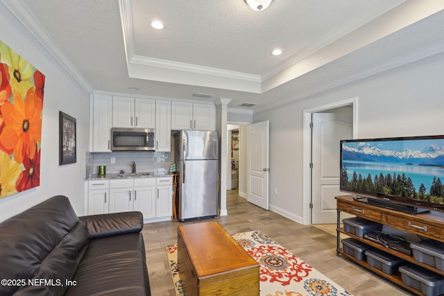 living room with light wood-type flooring, a raised ceiling, visible vents, and crown molding