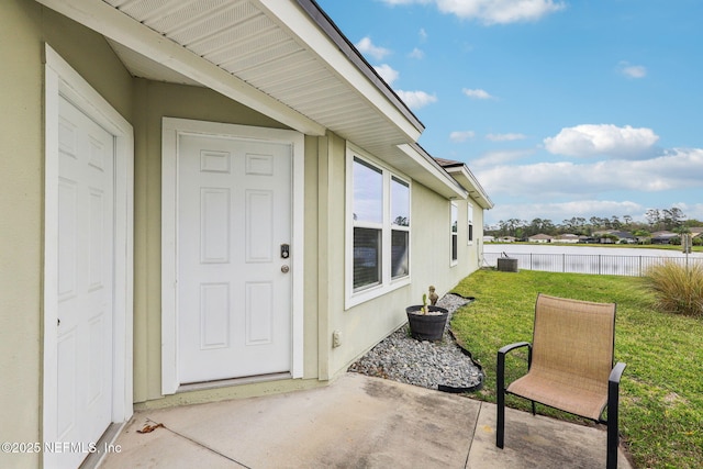 entrance to property featuring a patio, fence, a yard, stucco siding, and a water view