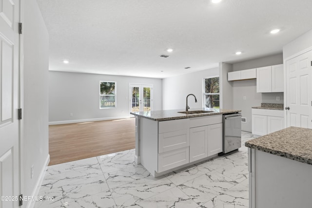 kitchen with sink, dark stone countertops, white cabinets, a center island with sink, and french doors