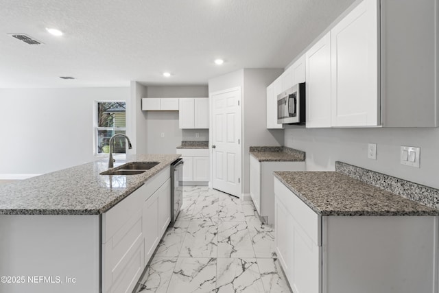 kitchen featuring white cabinetry, an island with sink, sink, dark stone countertops, and stainless steel appliances