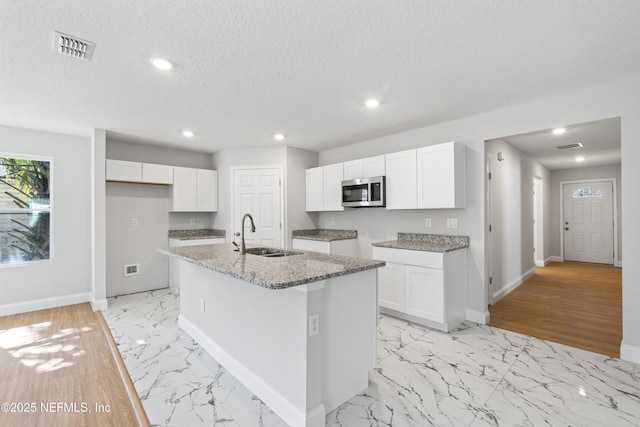 kitchen featuring sink, a textured ceiling, light stone countertops, a kitchen island with sink, and white cabinets