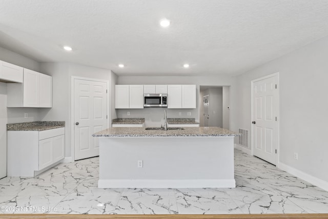 kitchen featuring stone countertops, a kitchen island with sink, sink, and white cabinets