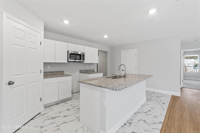 kitchen with an island with sink, sink, white cabinets, light stone countertops, and a textured ceiling