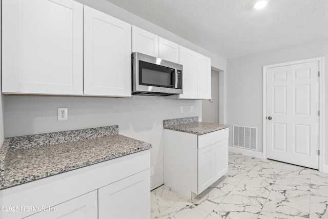 kitchen with light stone counters, white cabinets, and a textured ceiling