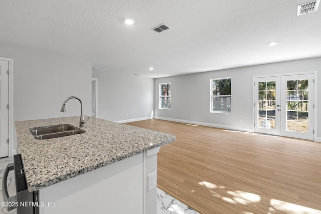 kitchen featuring a kitchen island with sink, sink, light hardwood / wood-style flooring, and a textured ceiling