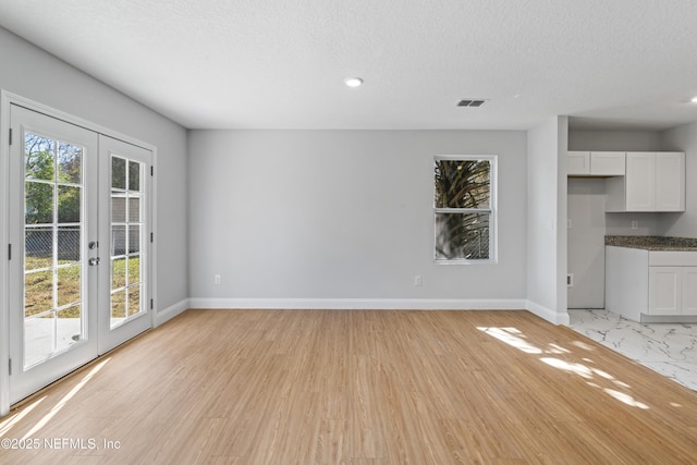 unfurnished living room with a textured ceiling, light wood-type flooring, and french doors