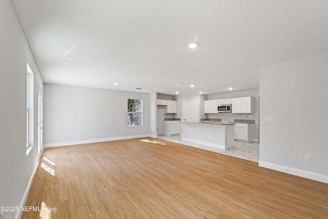 unfurnished living room featuring sink, a textured ceiling, and light wood-type flooring