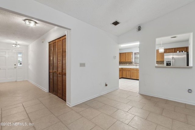 unfurnished room featuring light tile patterned floors, vaulted ceiling, and a textured ceiling