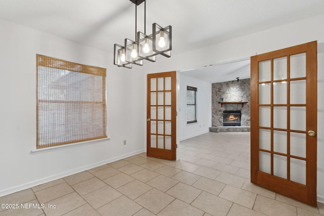 unfurnished dining area featuring a fireplace, a chandelier, light tile patterned floors, a textured ceiling, and french doors