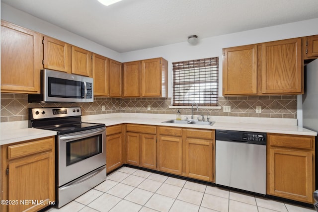 kitchen with light tile patterned flooring, appliances with stainless steel finishes, tasteful backsplash, sink, and a textured ceiling