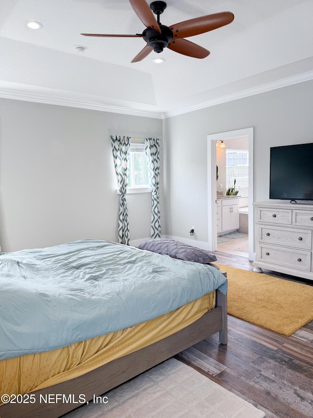 bedroom with ornamental molding, a tray ceiling, connected bathroom, and light hardwood / wood-style flooring