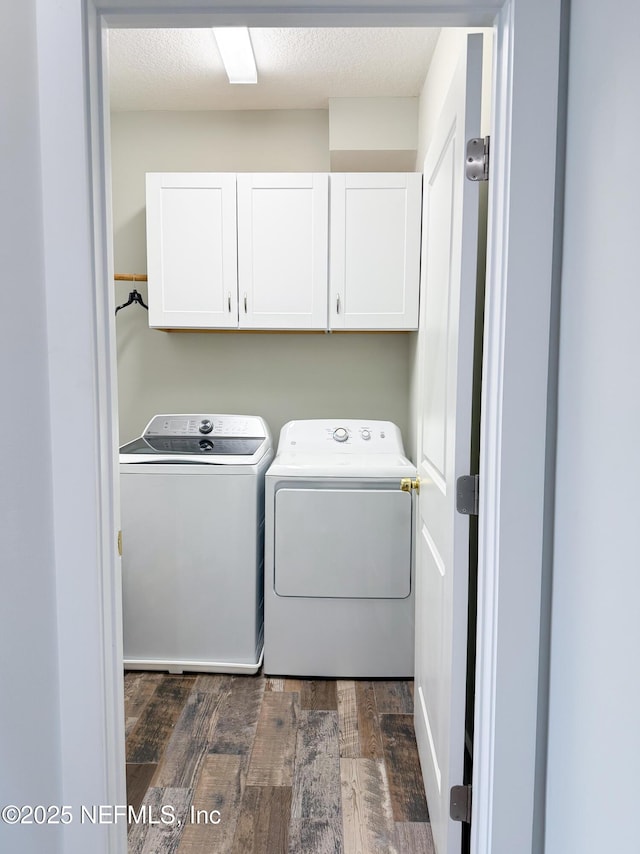 washroom featuring dark wood-type flooring, cabinets, washer and clothes dryer, and a textured ceiling