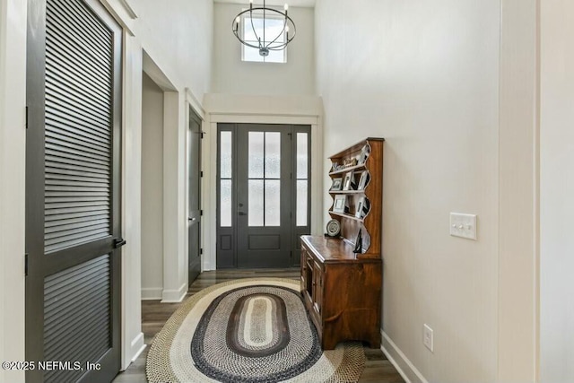 foyer entrance featuring dark wood-type flooring, an inviting chandelier, and a towering ceiling