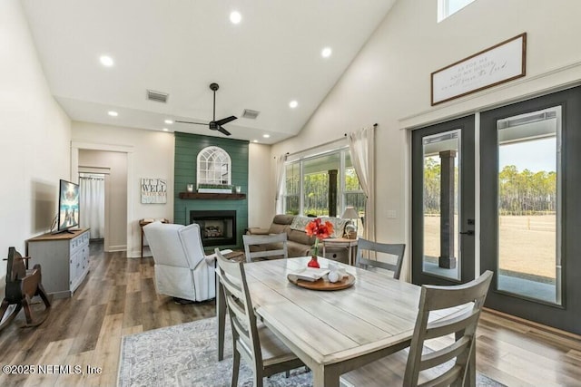 dining space featuring hardwood / wood-style flooring, ceiling fan, high vaulted ceiling, and a fireplace