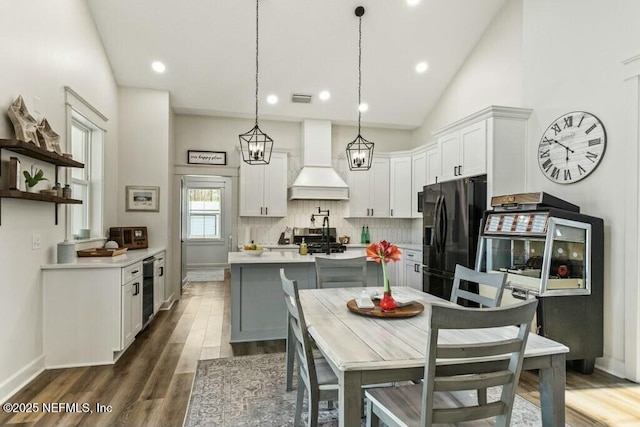 kitchen featuring premium range hood, black fridge, hanging light fixtures, white cabinets, and backsplash