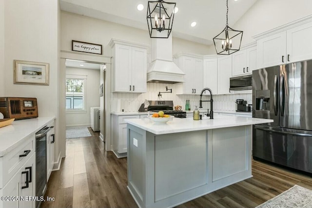 kitchen featuring appliances with stainless steel finishes, decorative light fixtures, white cabinetry, an island with sink, and custom range hood