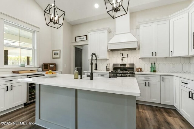 kitchen with white cabinetry, custom range hood, stainless steel range oven, a center island with sink, and decorative light fixtures