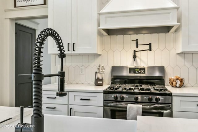 kitchen featuring custom exhaust hood, stainless steel gas range oven, backsplash, and white cabinetry