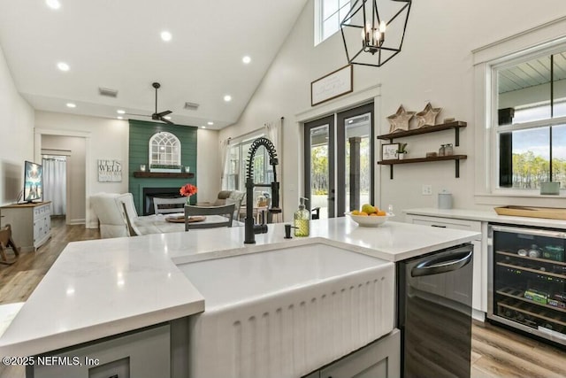 kitchen with sink, hanging light fixtures, wine cooler, a large fireplace, and light wood-type flooring