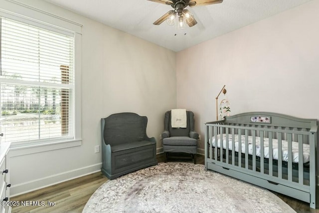 bedroom with a nursery area, ceiling fan, and wood-type flooring