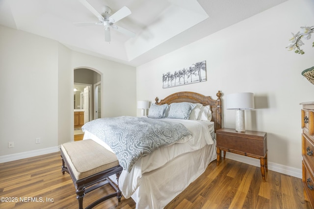 bedroom featuring arched walkways, a raised ceiling, baseboards, and wood finished floors