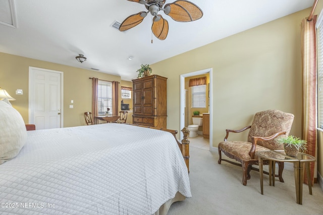 bedroom featuring visible vents, a ceiling fan, ensuite bath, baseboards, and light colored carpet