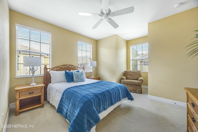 bedroom with multiple windows, light colored carpet, baseboards, and a ceiling fan