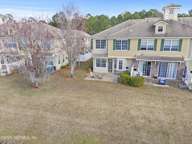 rear view of house featuring stone siding, a lawn, a tile roof, and a patio