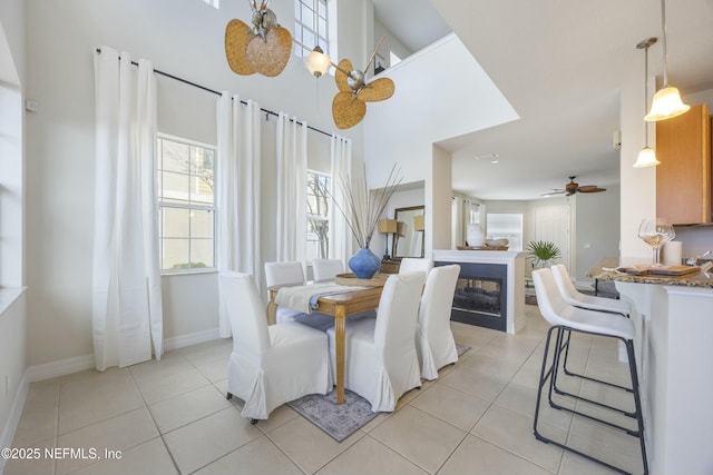 dining space featuring a glass covered fireplace, baseboards, light tile patterned flooring, and ceiling fan