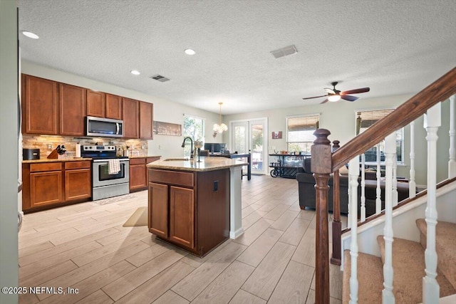 kitchen featuring sink, hanging light fixtures, a kitchen island with sink, light hardwood / wood-style floors, and stainless steel appliances