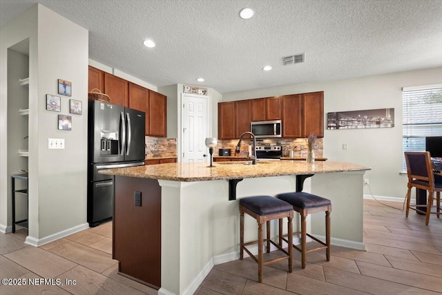 kitchen featuring sink, a kitchen island with sink, a kitchen breakfast bar, light stone countertops, and black fridge with ice dispenser