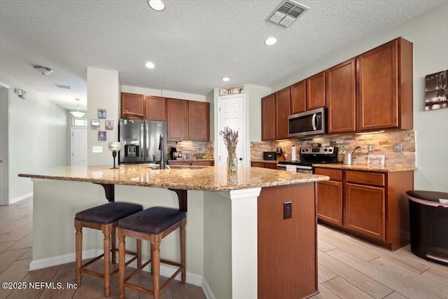 kitchen with light stone countertops, a breakfast bar, an island with sink, and appliances with stainless steel finishes