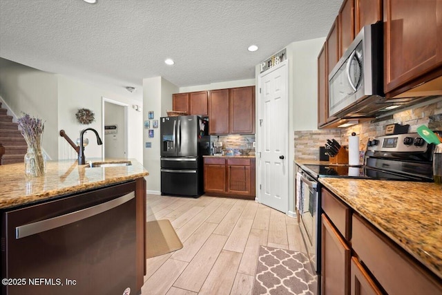 kitchen with light stone counters, sink, light hardwood / wood-style flooring, and appliances with stainless steel finishes