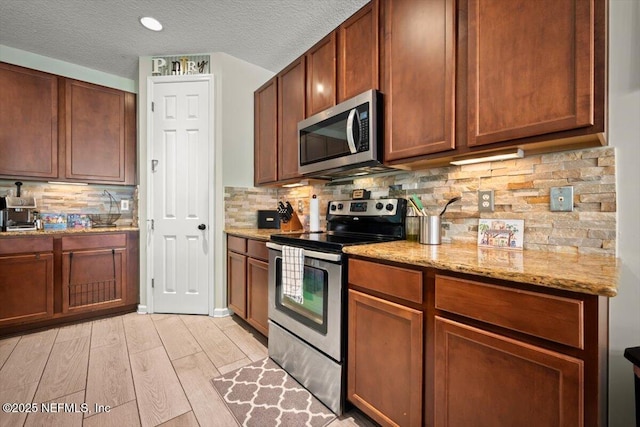 kitchen featuring light stone counters, a textured ceiling, stainless steel appliances, light hardwood / wood-style floors, and backsplash