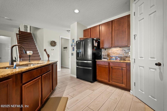 kitchen with sink, backsplash, light stone counters, light hardwood / wood-style floors, and black refrigerator with ice dispenser