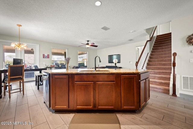 kitchen featuring light stone countertops, sink, a kitchen island with sink, and decorative light fixtures