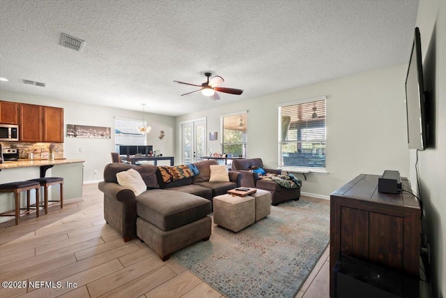 living room featuring ceiling fan, light hardwood / wood-style floors, and a textured ceiling