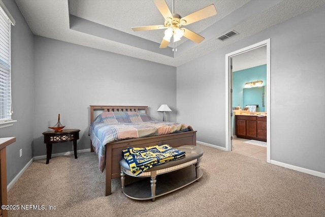 bedroom featuring ceiling fan, connected bathroom, a textured ceiling, light colored carpet, and a raised ceiling