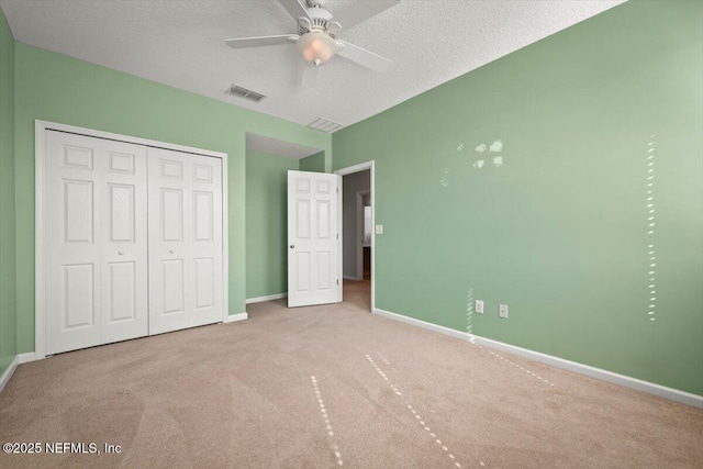 unfurnished bedroom with ceiling fan, light colored carpet, a textured ceiling, and a closet