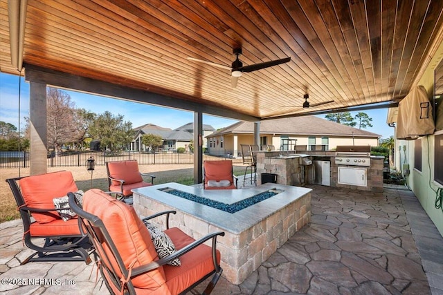 view of patio with area for grilling, an outdoor fire pit, an outdoor wet bar, ceiling fan, and exterior kitchen