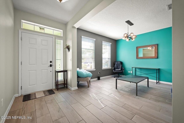 entrance foyer with an inviting chandelier, a textured ceiling, and light wood-type flooring